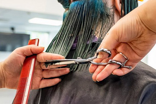Students using a comb and scissors to cut blue hair during one of her hairdressing courses